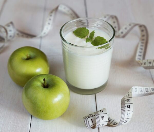 a glass of milk next to two green apples and a measuring tape